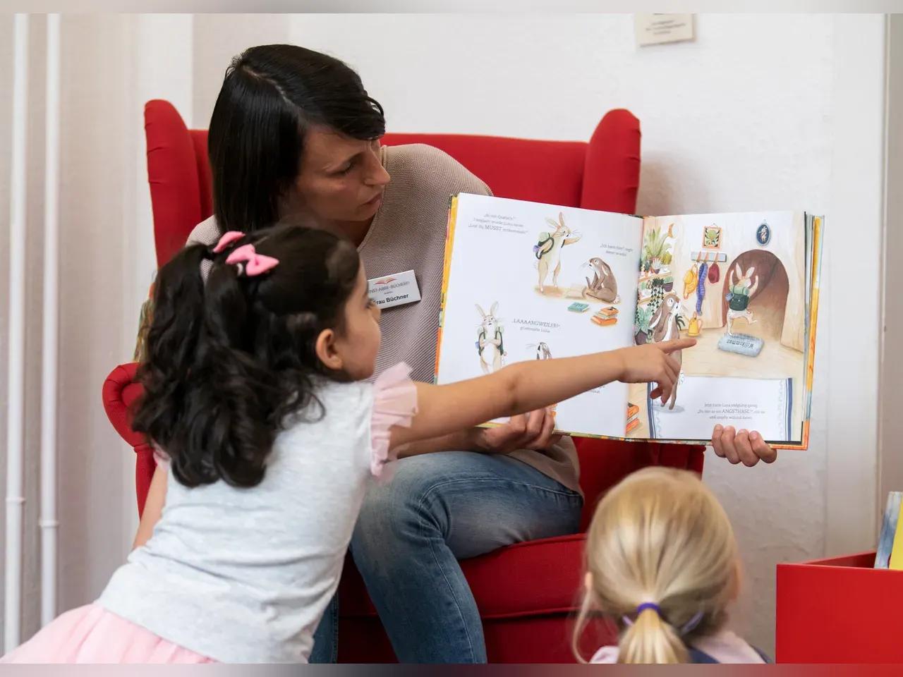 Frau in einem roten Sessel ließt zwei Mädchen ein Buch vor