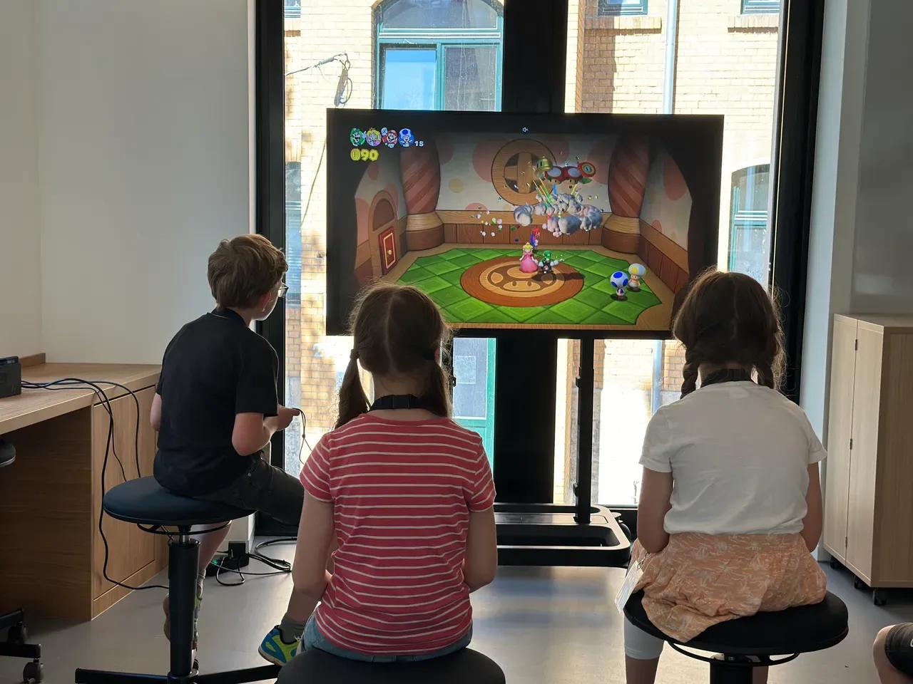 Kinder gamen an einem großen Bildschirm