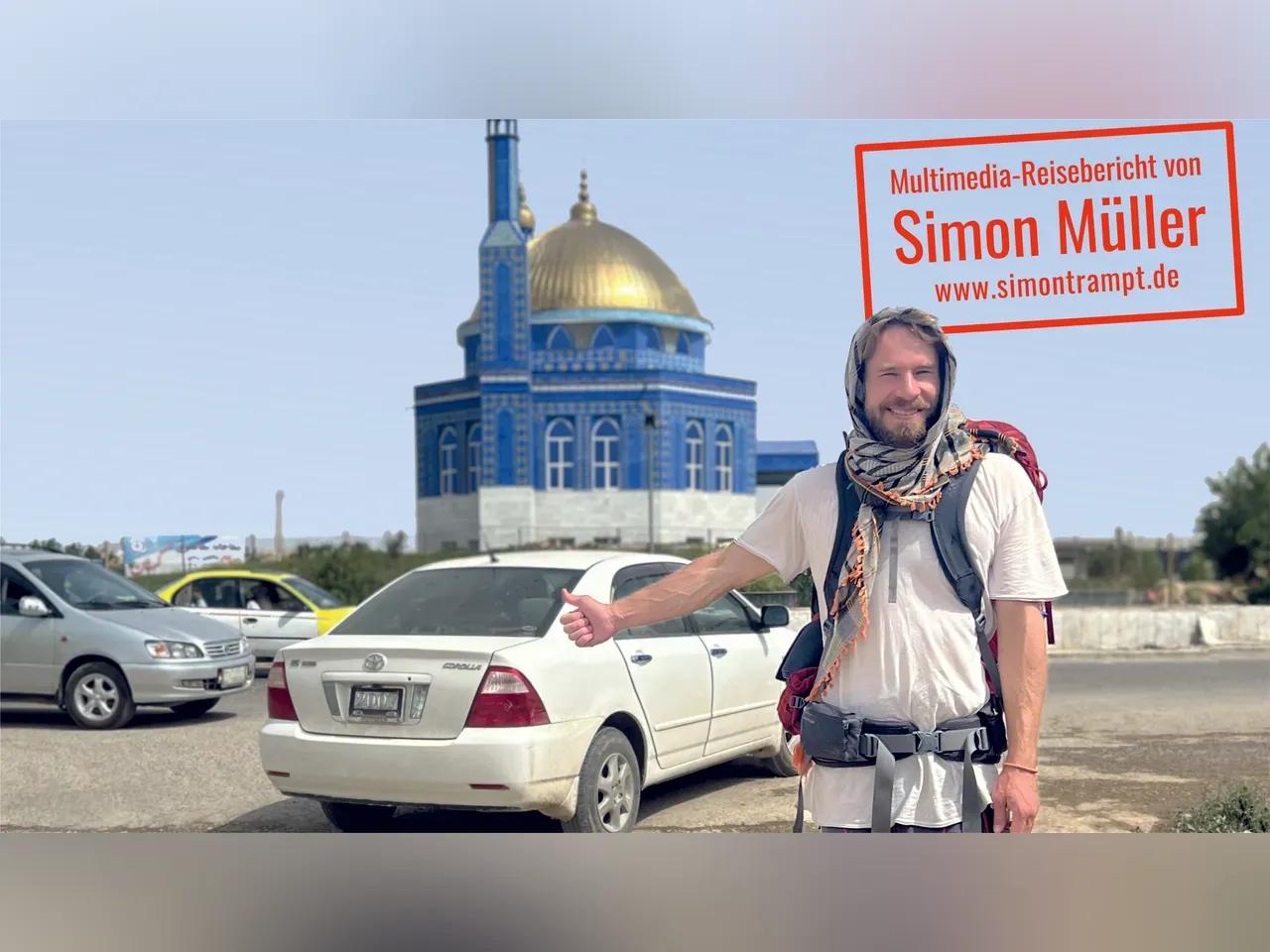 Simon Müller steht mit Daumen nach oben vor einem Auto und einer Moschee