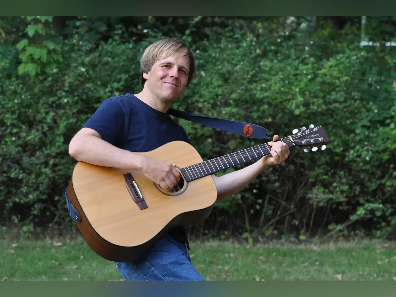 Christian Schmiedt mit seiner Gitarre im Grünen