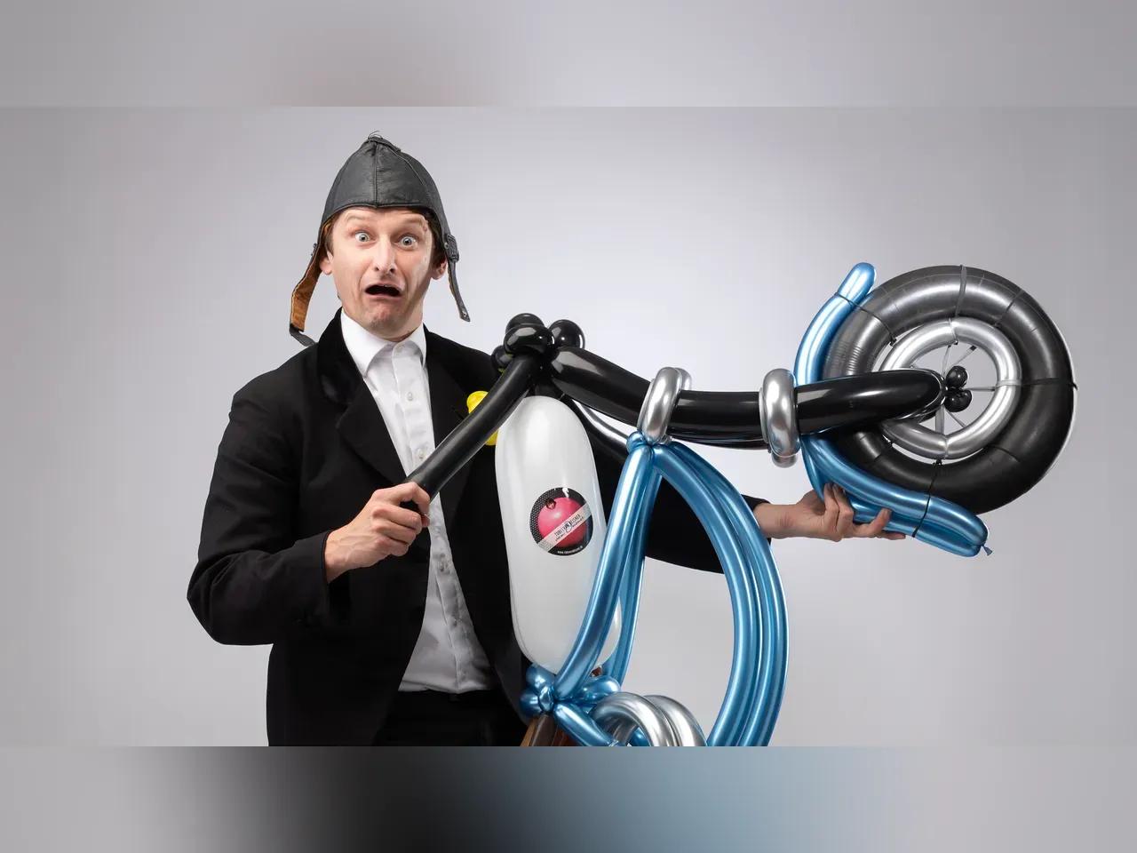 Ein Mann mit lederner Fliegerkappe sitzt auf einem Luftballon-Motorrad und sieht entsetzt aus.
