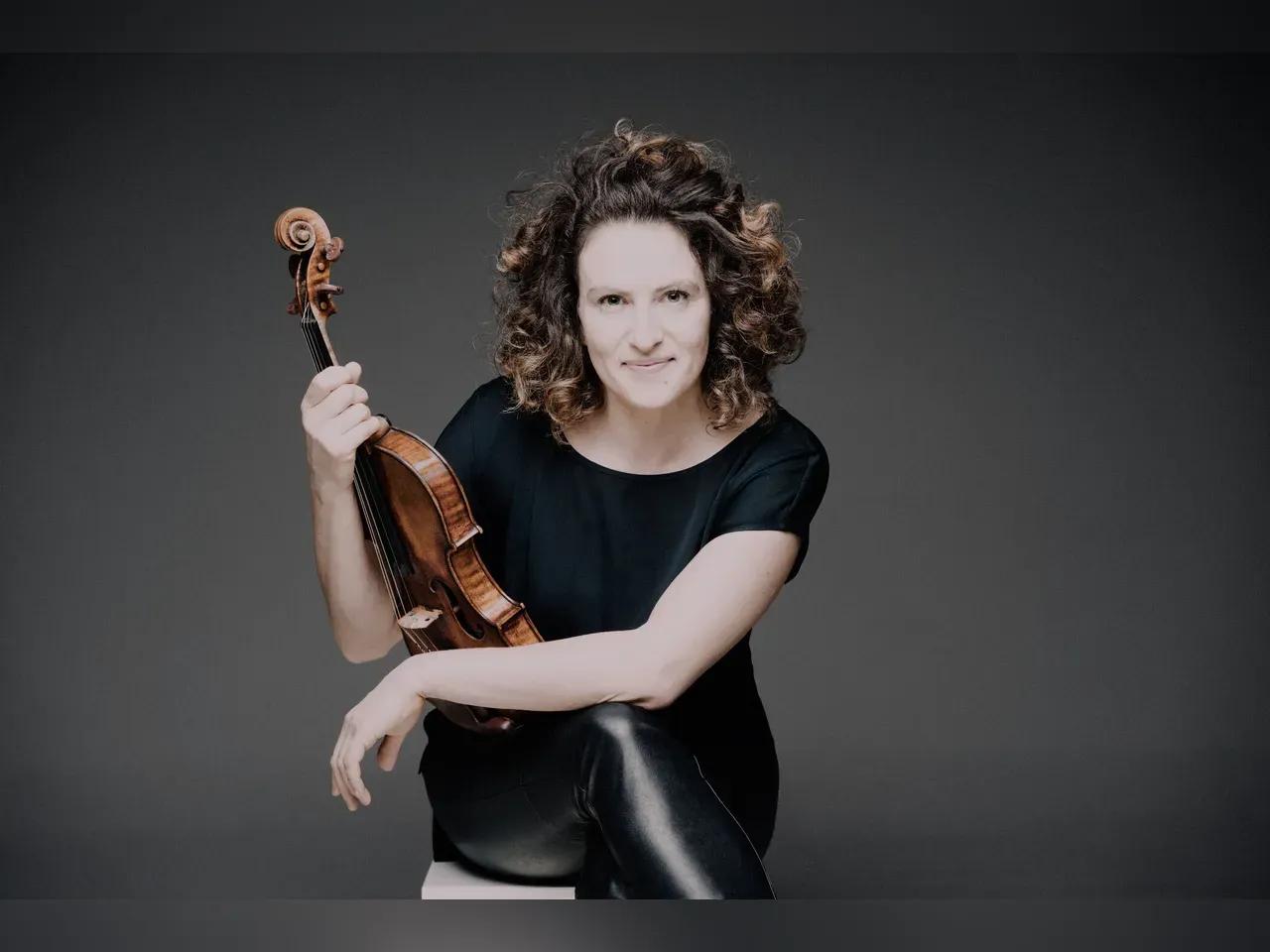 Porträtfoto der Violinistin Liza Ferschtman. Sie sitzt auf einem Hocker und hält ihre Violine in der Hand.