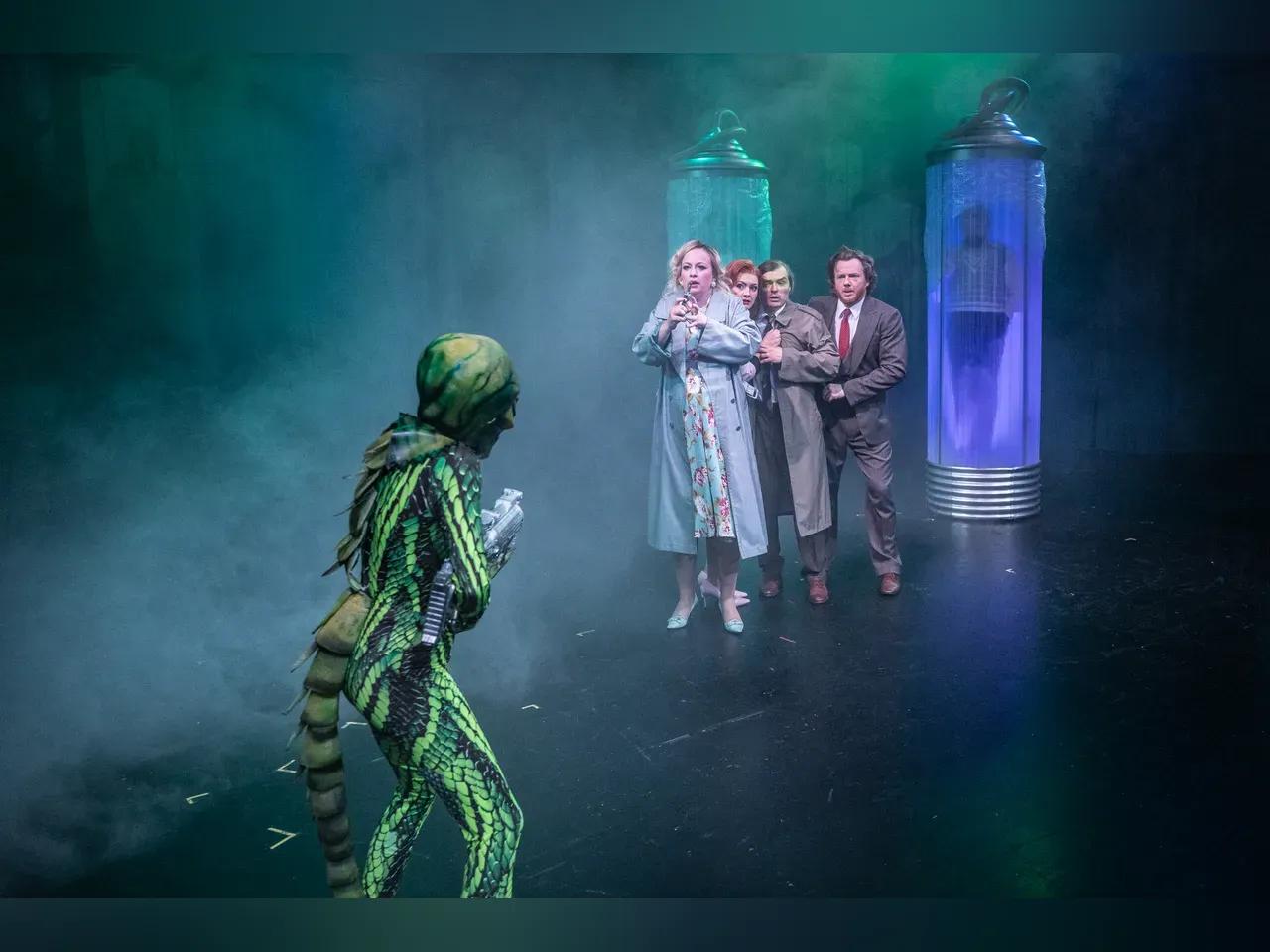 Eine Gruppe von Schaustellern wird während einer Vorstellung von einem Alien mit Waffe bedroht