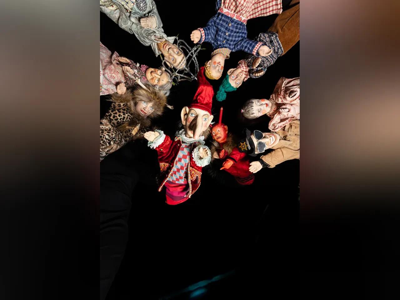 Eine Gruppe von Puppen schaut vor einem schwarzem Hintergrund in die Kamera