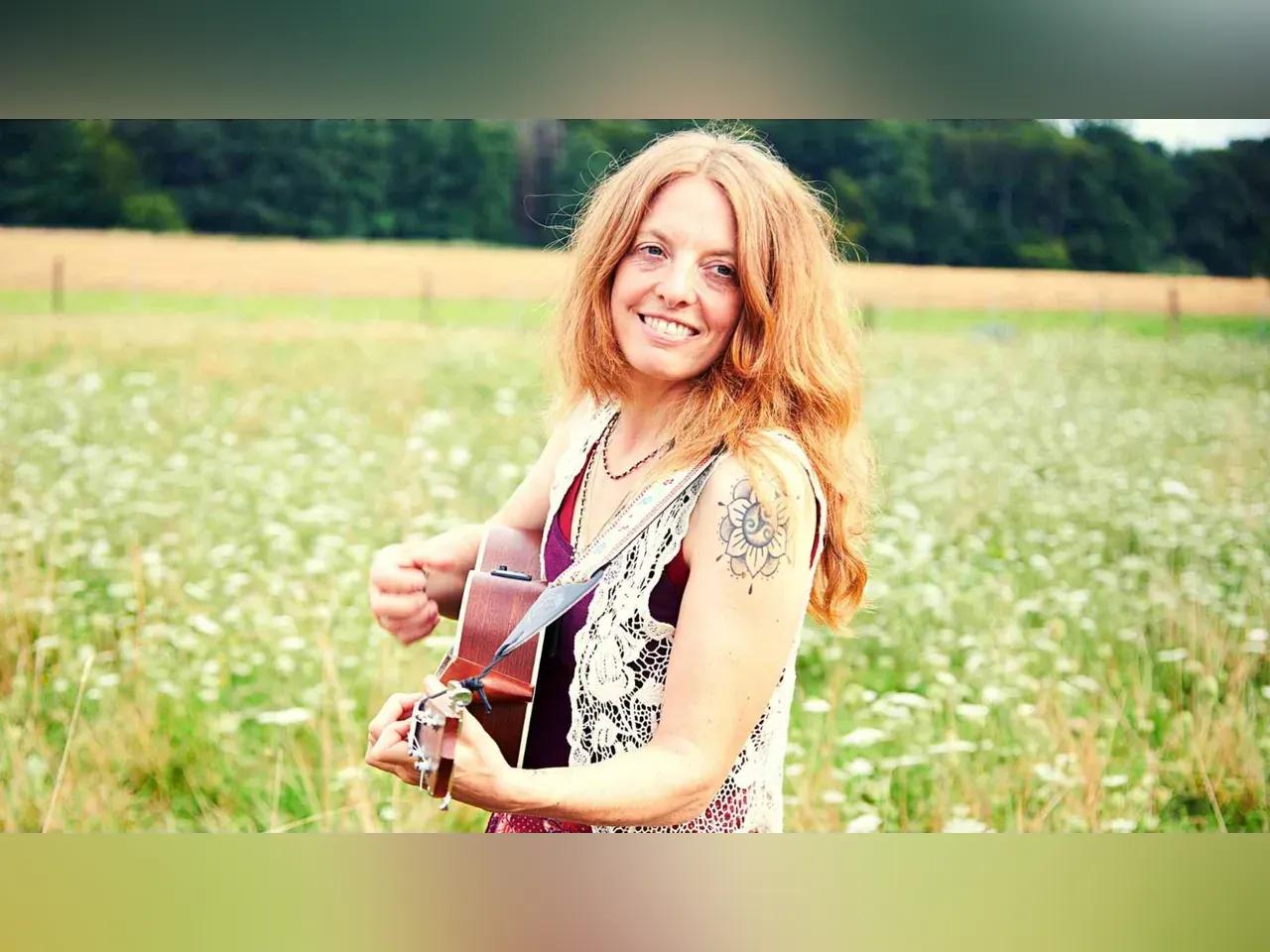 Eine Frau steht mit einer Gitarre in einer Blumenwiese.