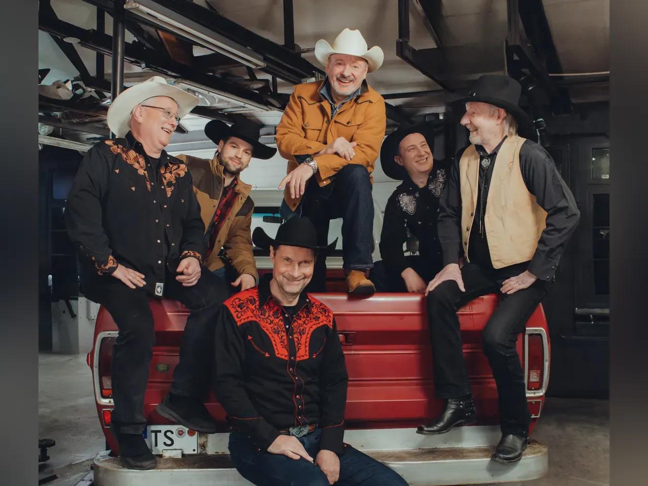 Die 6 Musiker der Band Truckstop posieren mit Cowboyhüten auf der Ladefläche eines Autos