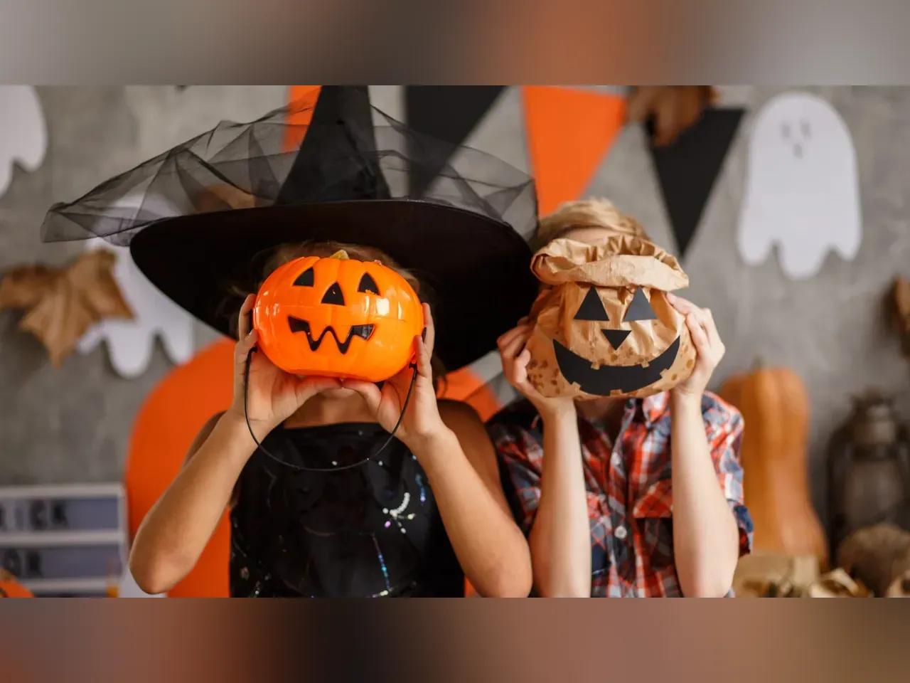 Zwei Kinder, die Halloween-Kürbisse vor das Gesicht halten und im Hintergrund sieht man Halloweendeko.