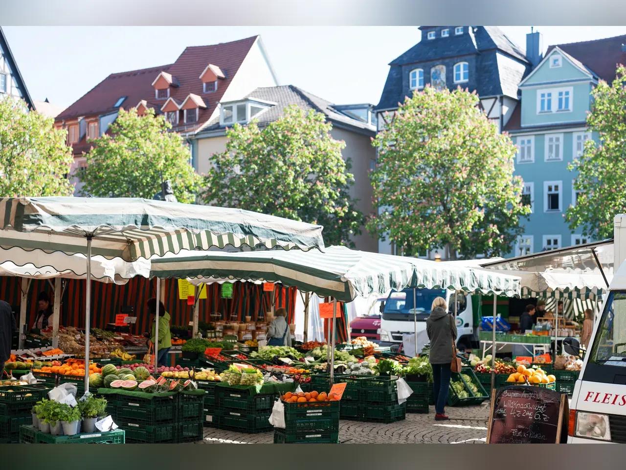 Stand auf dem Jenaer Wochenmarkt mit Kisten voll Gemüse und Obst, dazwischen Kunden und ein Händler