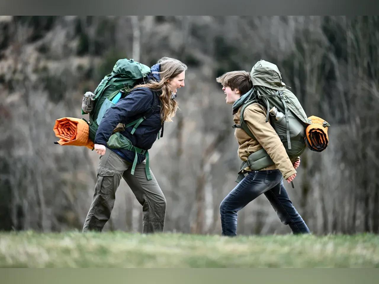 Zwei Wanderer:innen stehen mit viel Gepäck auf dem Rücken auf einer Wiese und schreien sich an