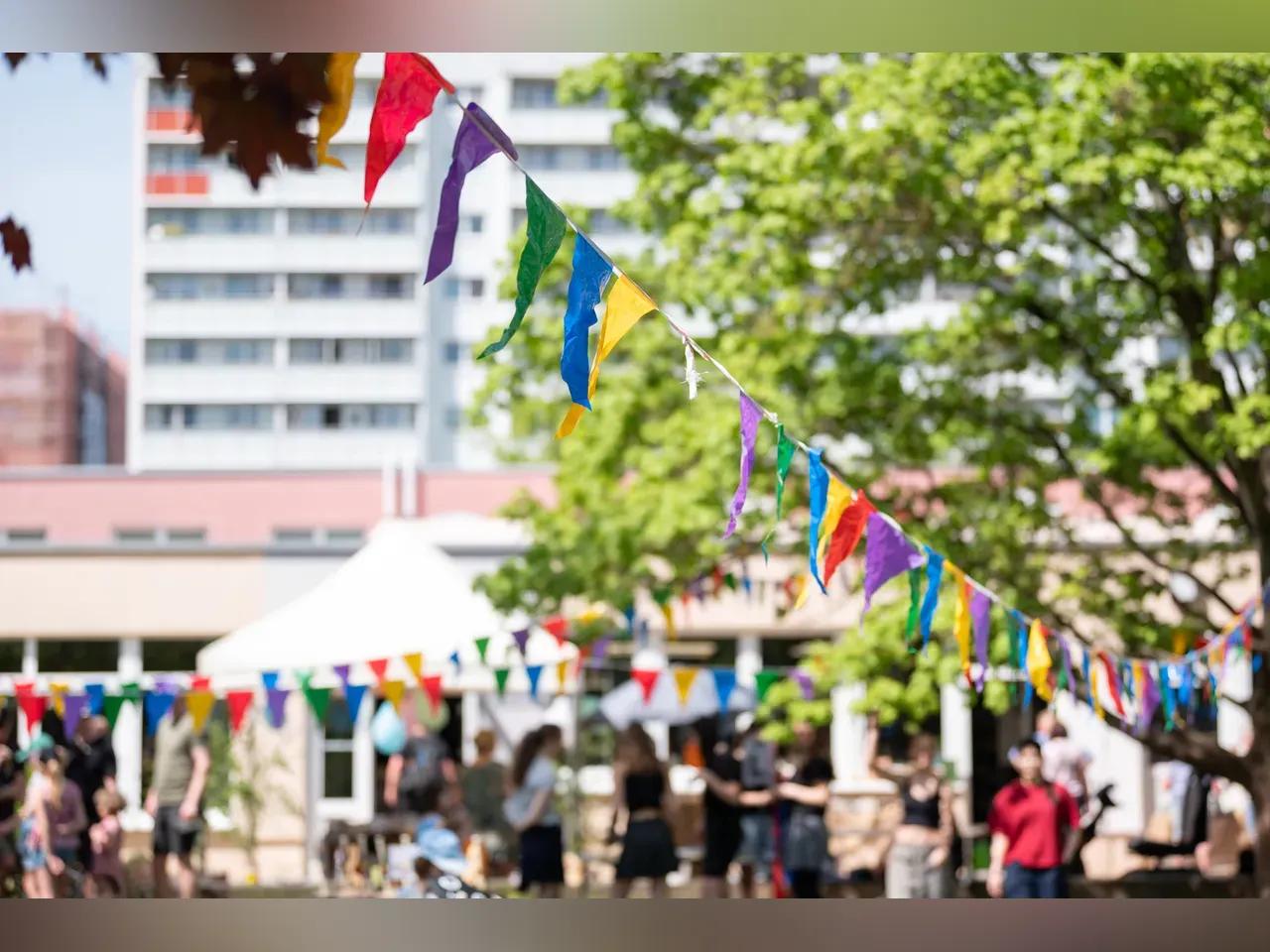 bunte Wimpel im Vordergrund und im Hintergrund Gäste, die das Gartenfest feiern, und ein Gebäude sowie Hochhäuser