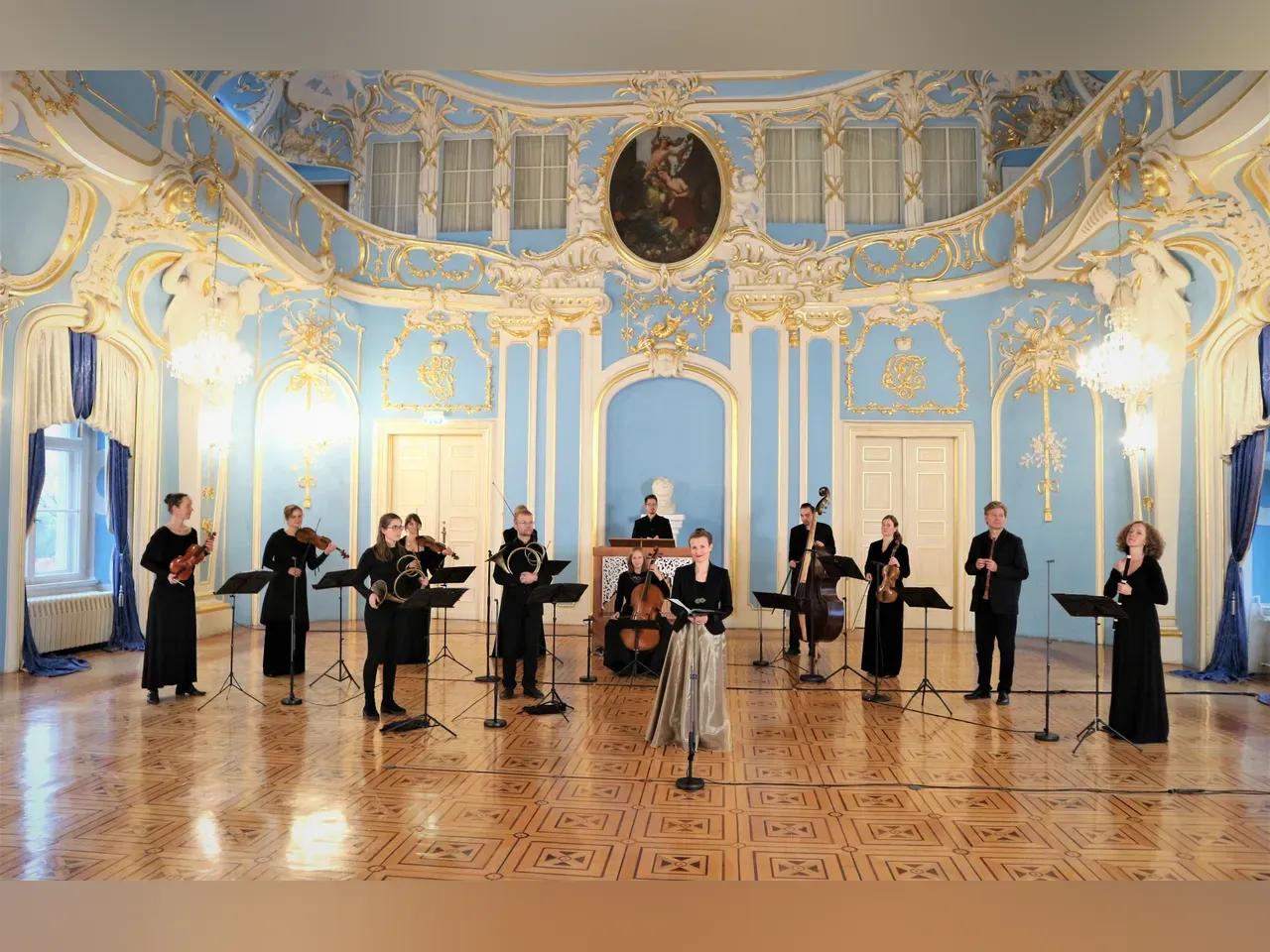 Festlich gekleidete Musiker:innen mit klassischen Instrumenten und Notenständern in einem prunkvollen barocken Saal