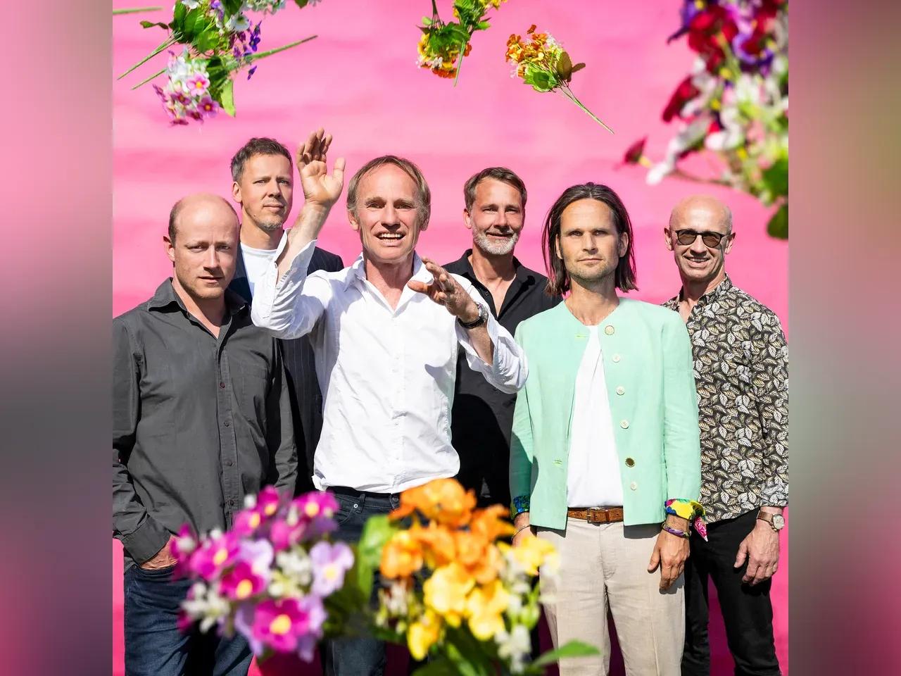 Die 6 Musiker und umherfliegende Blumen vor rosa Hintergrund