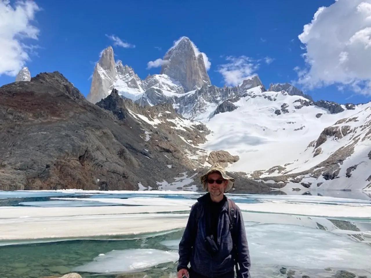 im Vordergrund ein Mensch, im Hintergrund ein See mit Eisplatten und schneebedeckten Bergen