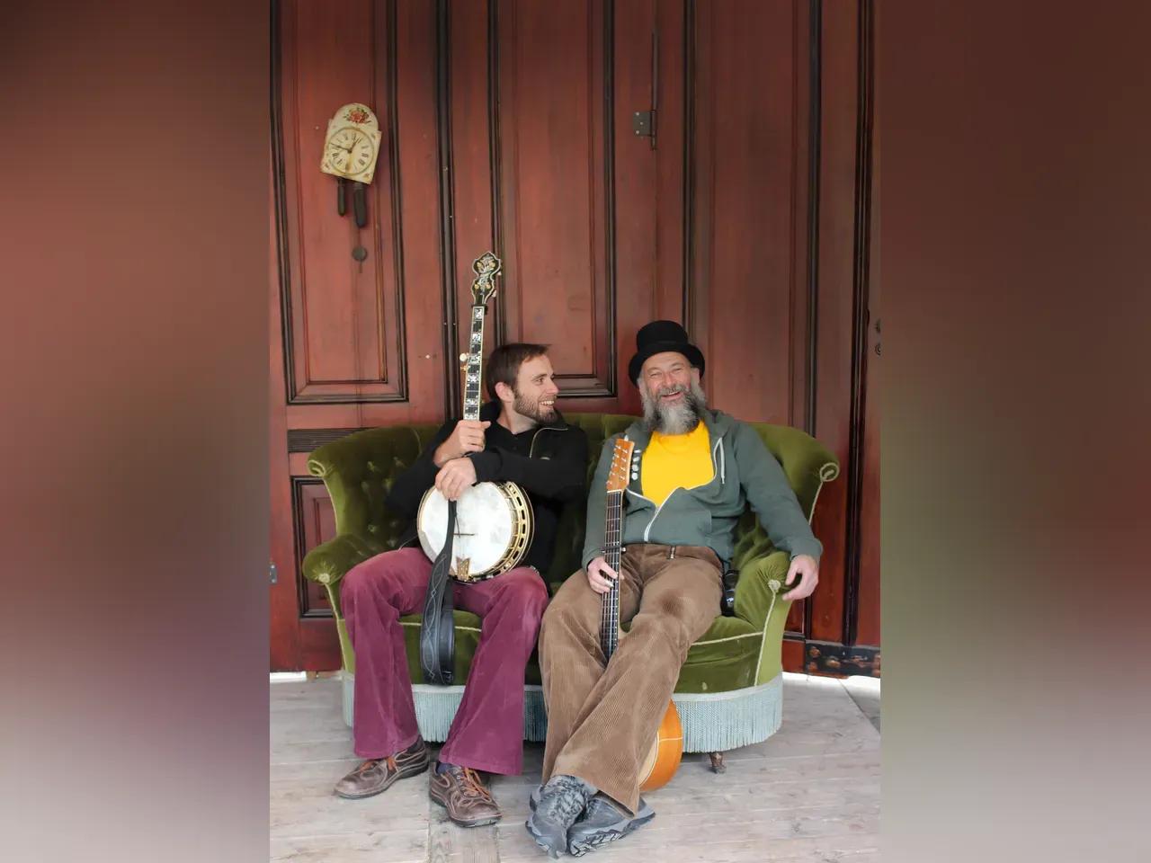 2 Musiker mit Banjo und Gitarre auf einem Sofa