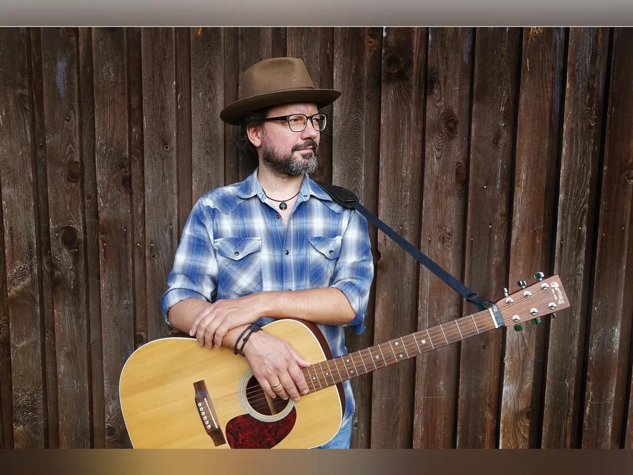 Tobias Panwitz mit Gitarre vor einer Bretterwand