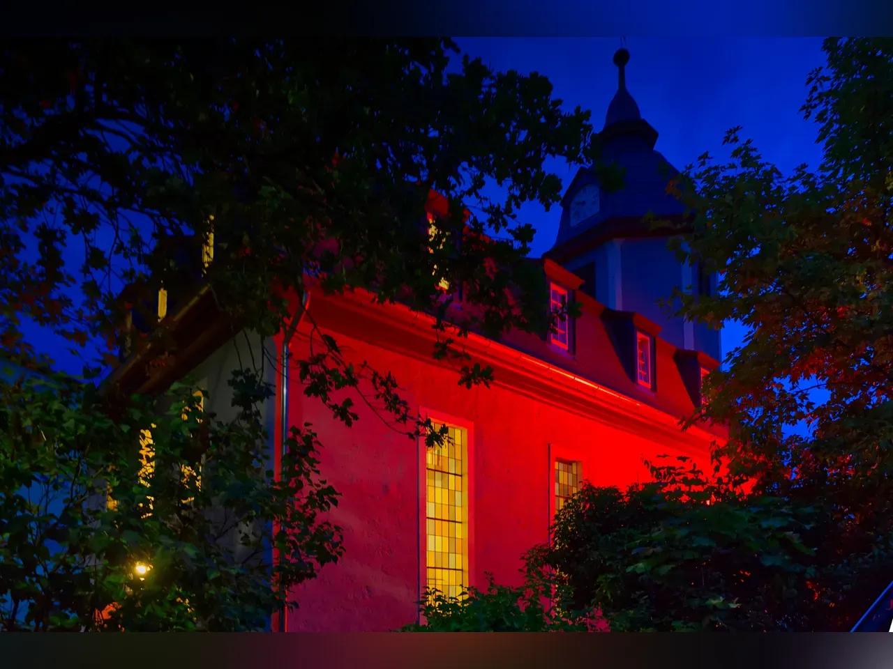 Kirchengebäude von außen rot angestrahlt, von innen erleuchtet