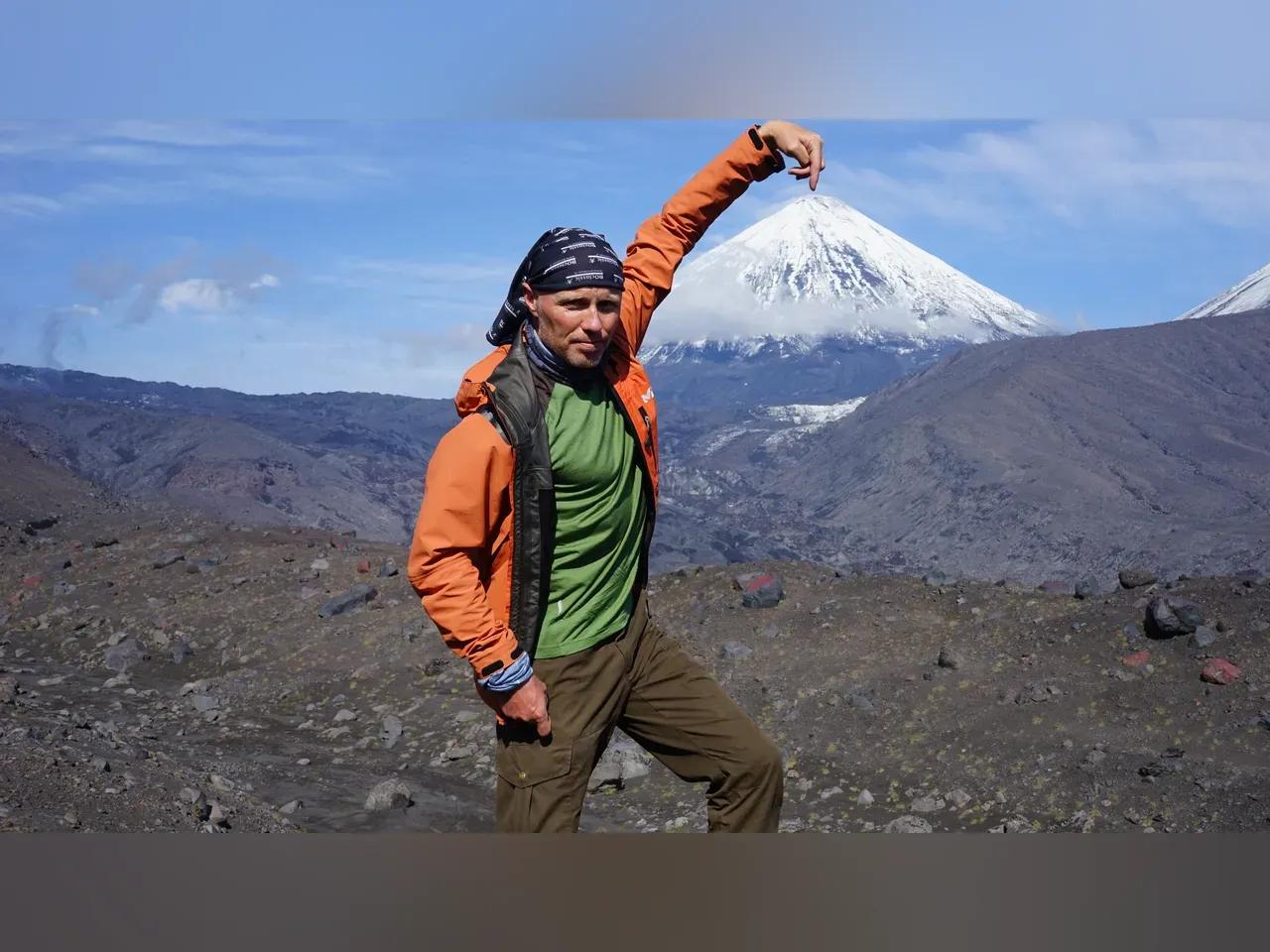 Reiseenthusiast Ralf Schwan posiert vor einem Berg mit schneebedeckter Kuppe in Kamtschatka.
