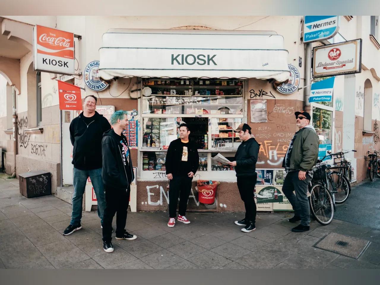 Bandmitglieder von Lagwagon stehen vor einem Kiosk