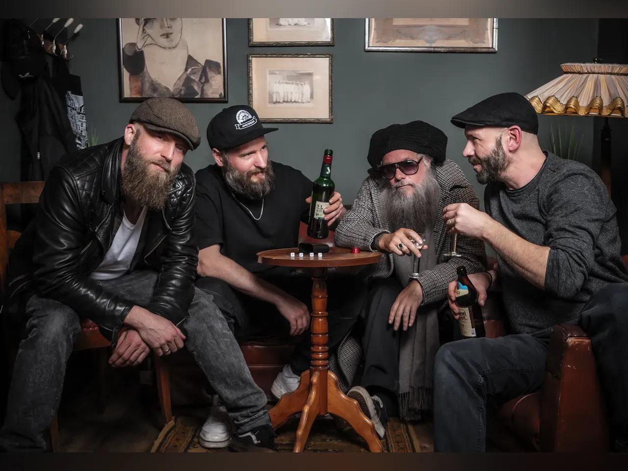 Bandmitglieder von Jaya the Cat sitzen in einem altmodischen Raum um einen kleinen Tisch und trinken