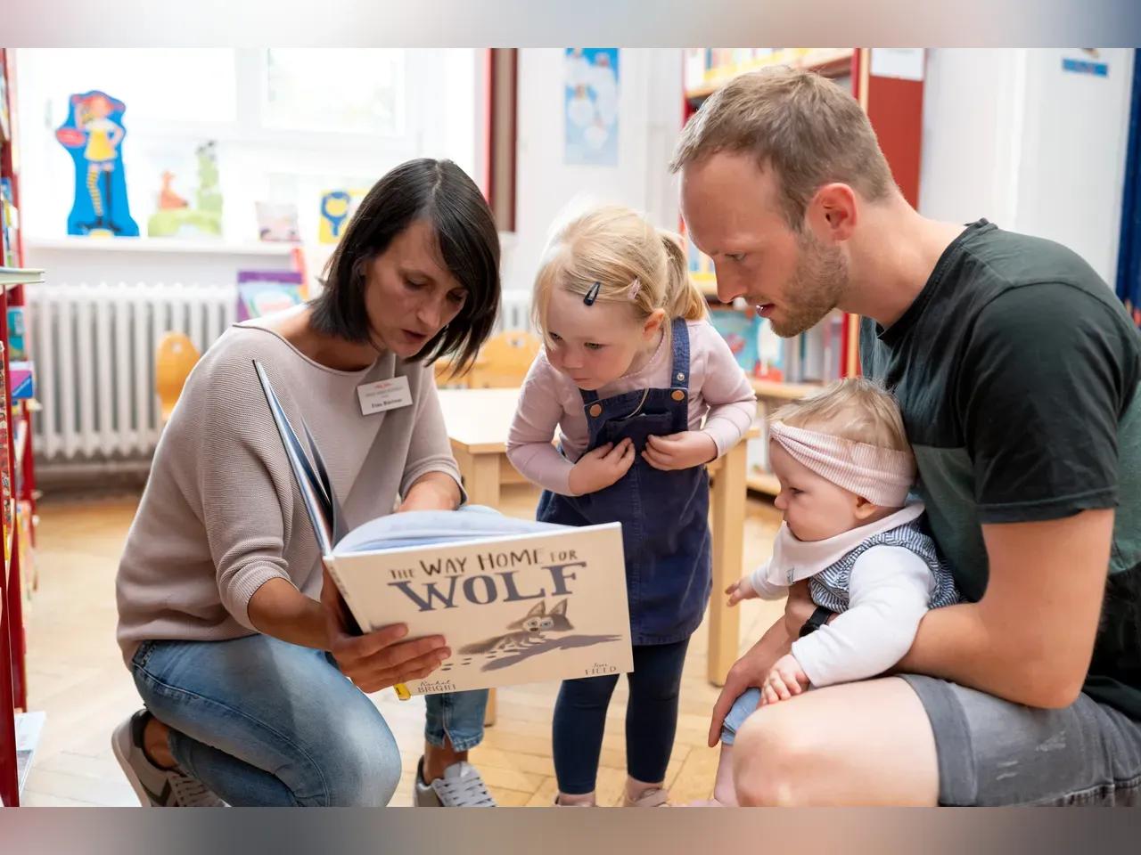 Frau liest mit zwei Kindern und Papa ein Buch