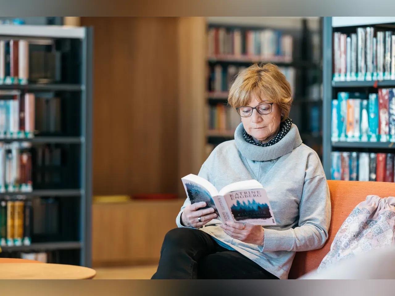 Eine ältere Frau sitz auf einem Sofa im Belletristik-Bereich der EAB und ließt in einem Buch
