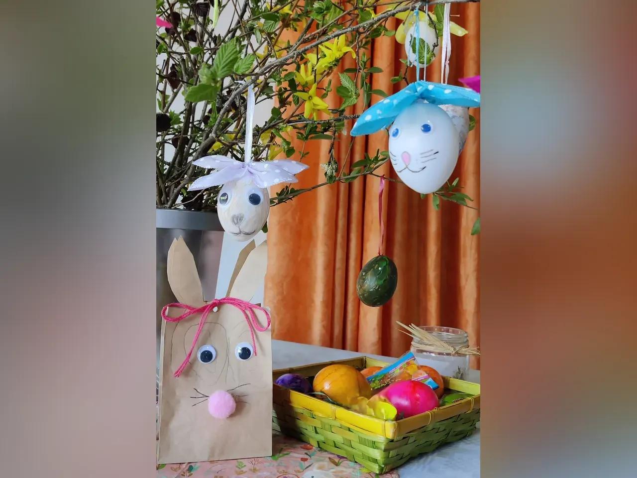 Ein Osterstrauß links im Bild, an dem Ostereiner hängen. Im Vordergrund steht ein Osterkörbchen mit bunten Eiern.