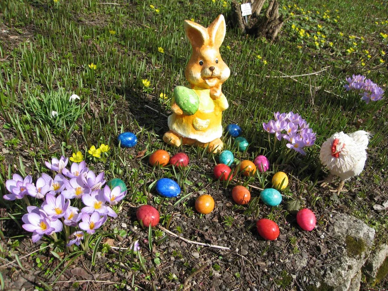 Osterhase mit bunt gefärbten Ostereiern, einem Huhn und blühenden Krokussen auf der Wiese