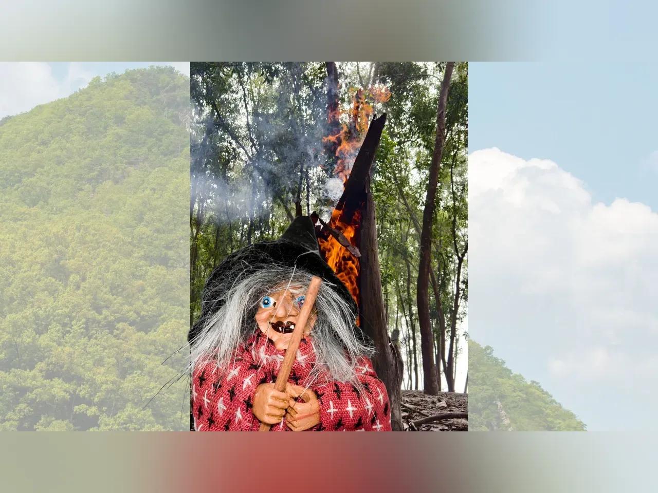 Im Hintergrund ein Berg, davor eine Hexenpuppe im Wald mit einer Fackel in den Händen