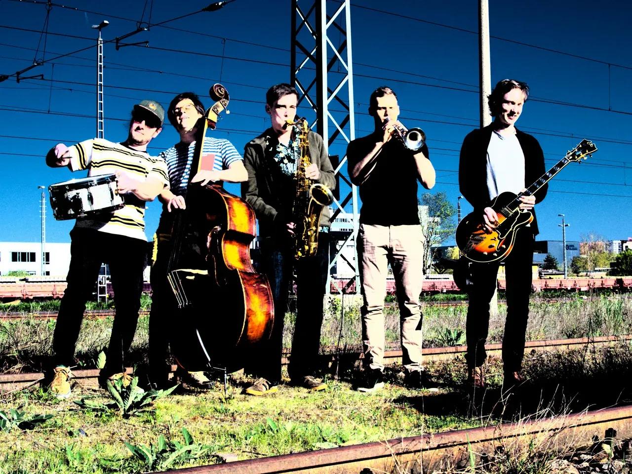 Vier Musiker:innen mit Instrumenten an einem Bahngleis