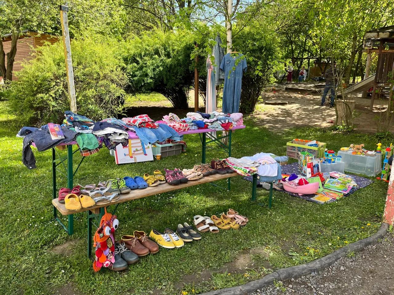Flohmarktstand auf einer Wiese mit ausgestellten Schuhen, Kleidung und Spielsachen