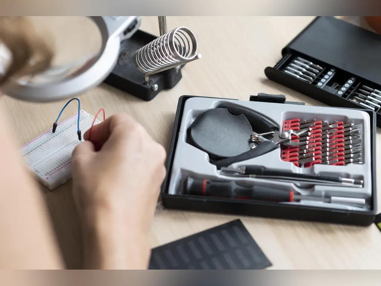 Eine Person lötet auf einer Platine. Im Hintergrund stehen hierzu das passende Werkzeug bereit.