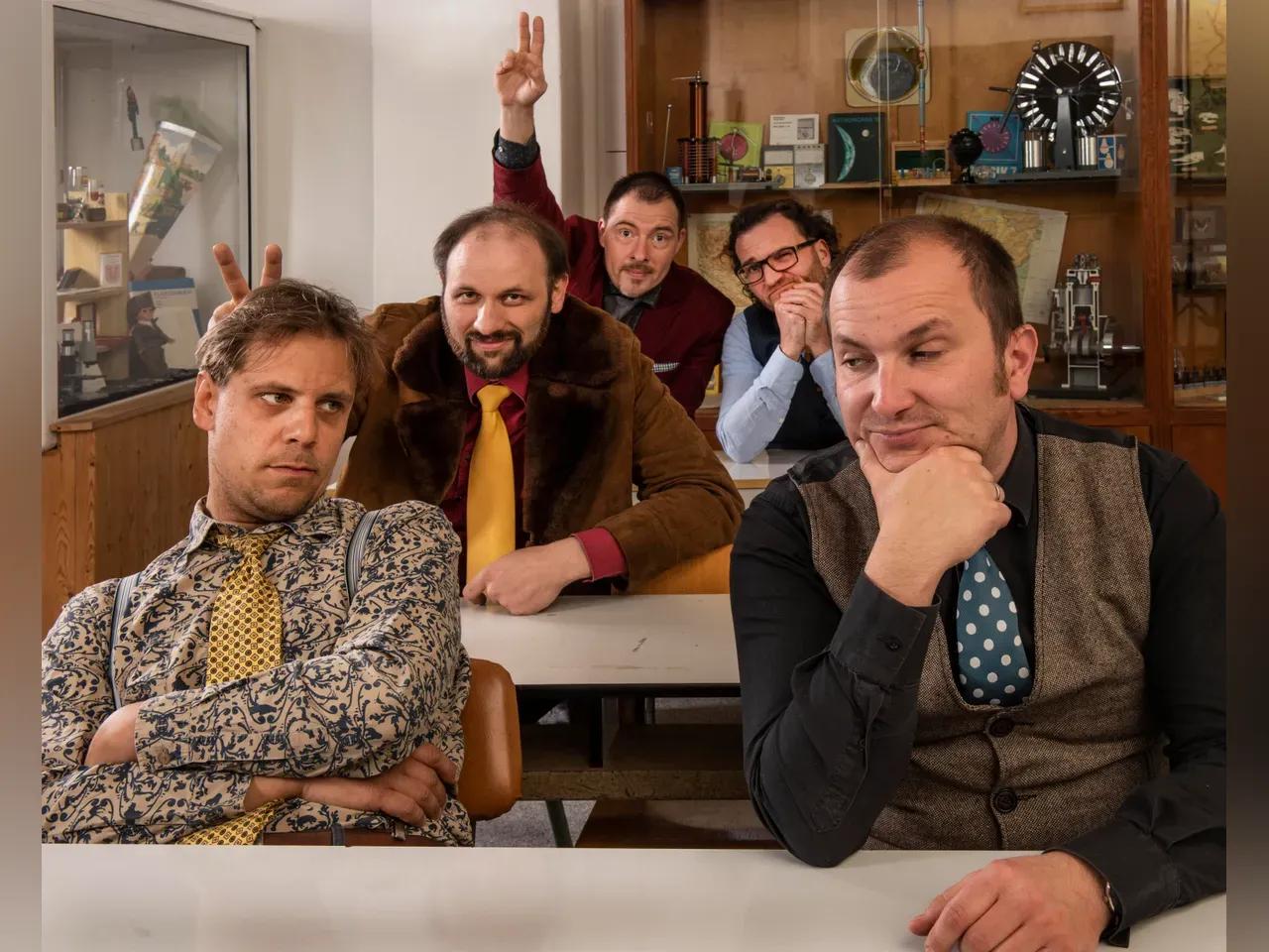 Die Musiker von B 1000 sitzen an alten Schultischen