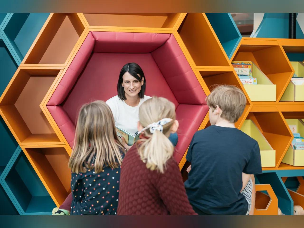 Frau mit braunen Haaren liest Kindern ein Buch vor