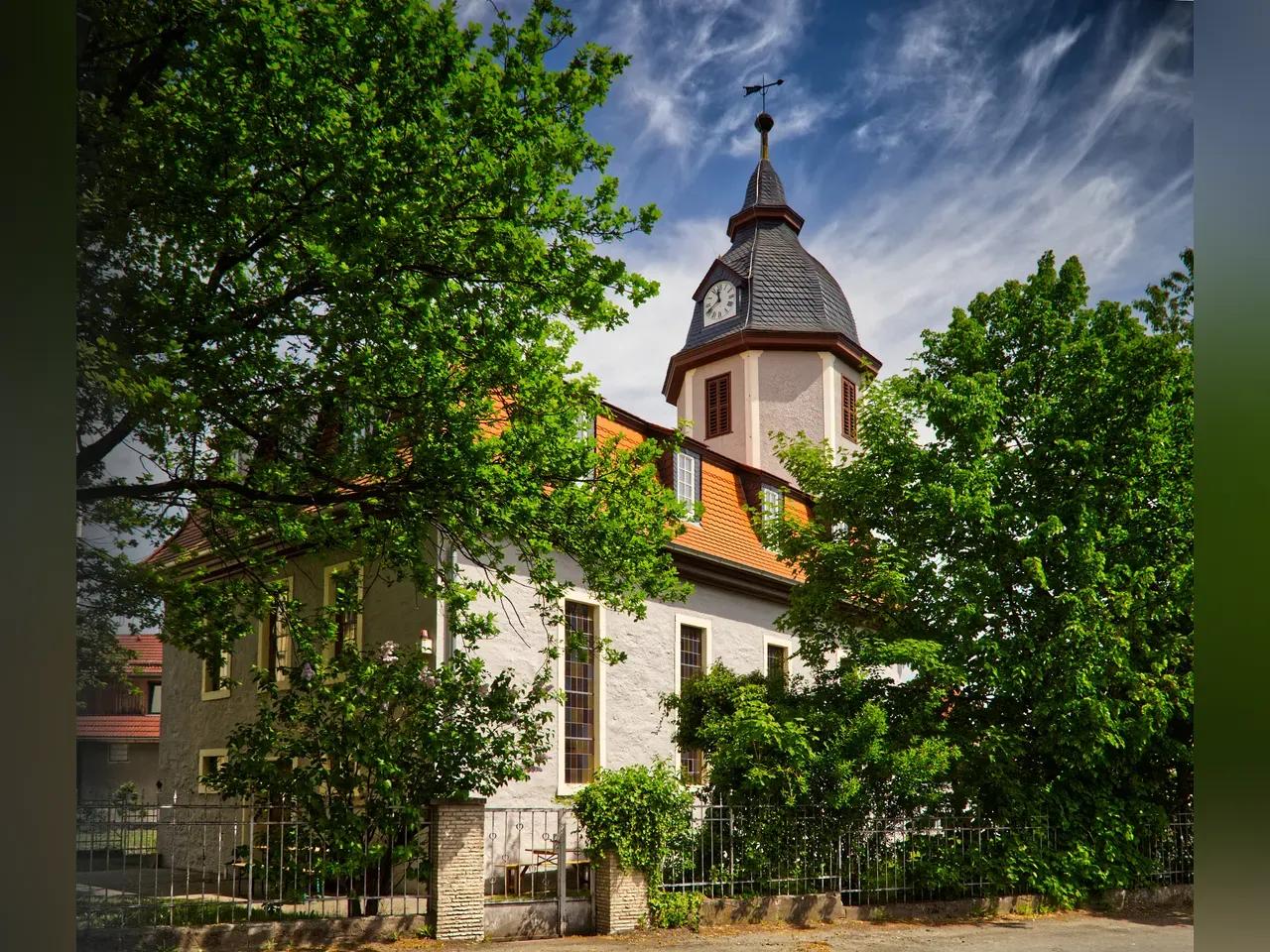 Außenansicht der KulturKirche Löbstedt mit grünen Bäumen und blauem Himmel