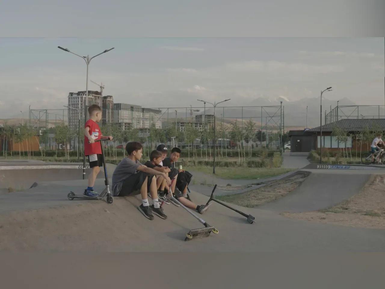 fünf Jungs, teilweise mit Roller, befinden sich zusammen auf einem Skatepark