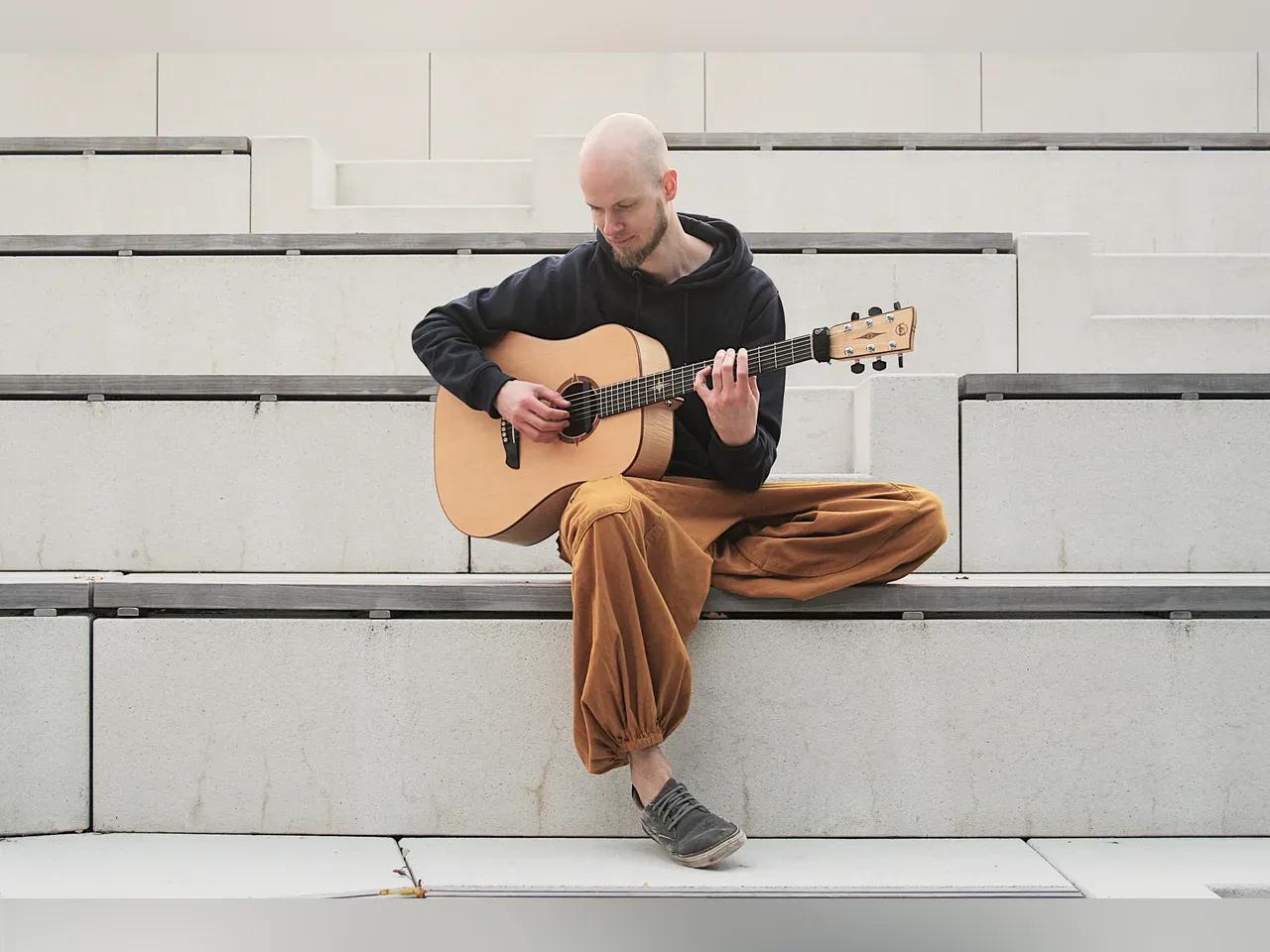 Robert Graefe sitzt mit seiner Gitarre auf einer Bank aus Beton