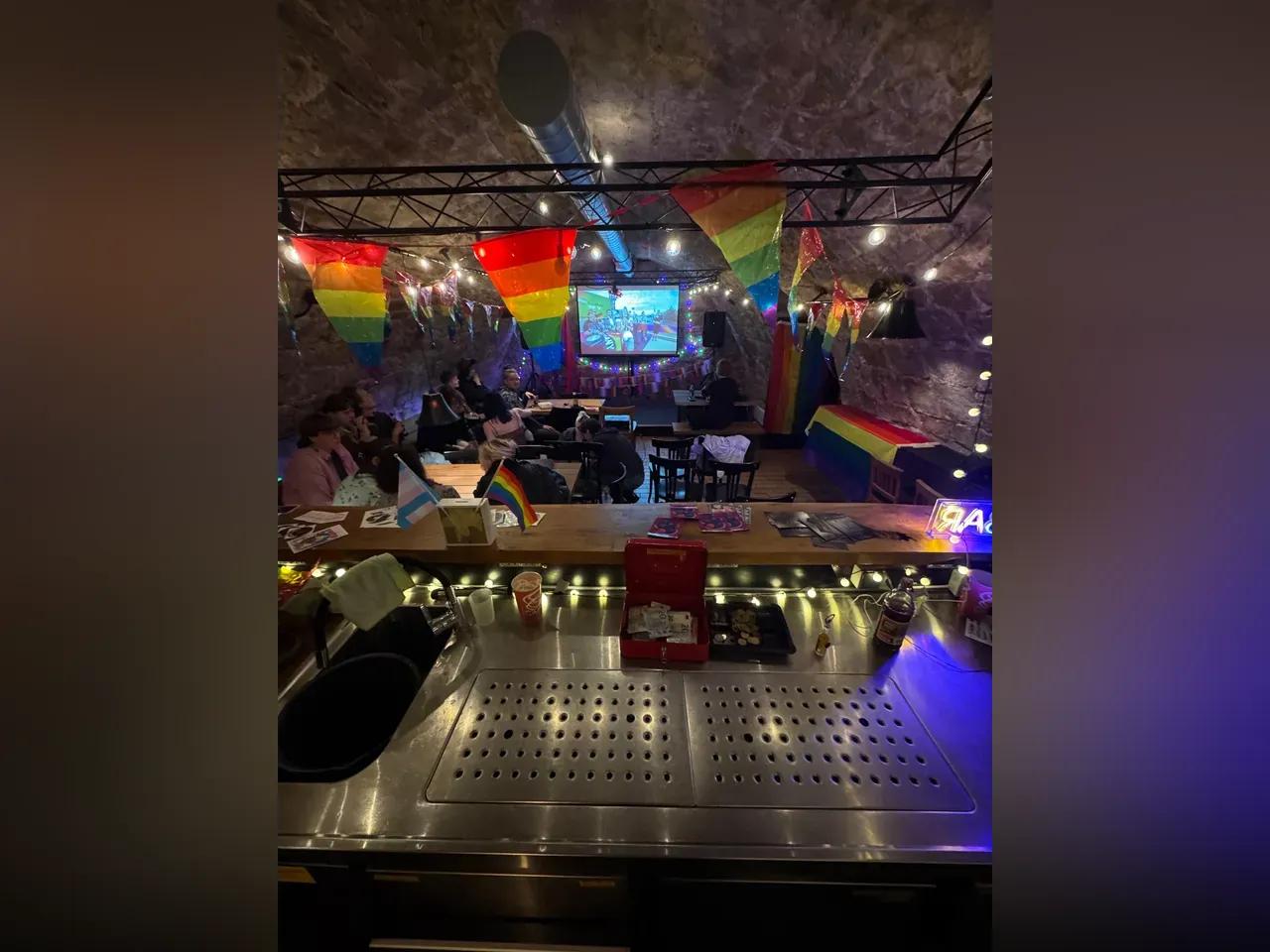 Blick in einen Kneipenkeller, der mit Pride-Fahnen und Lichterketten dekoriert ist