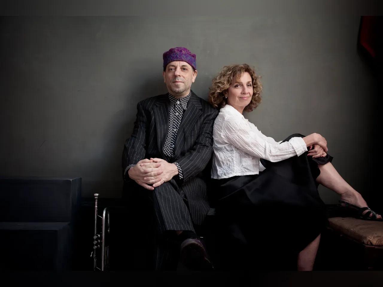 Eleanor Reissa und Frank London sitzen aneinander gelehnt vor einer Wand und schauen in die Kamera