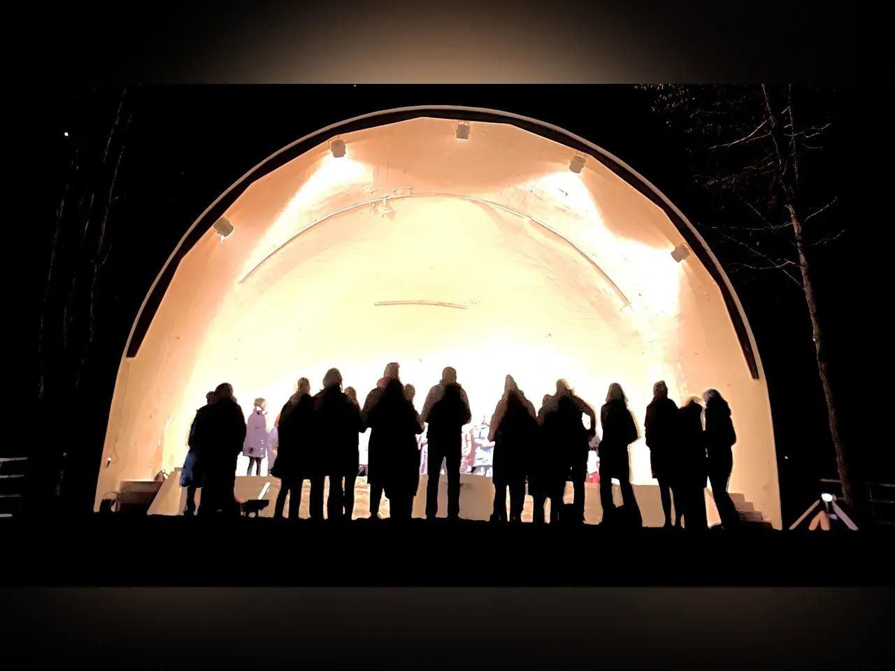 Silhouetten von Menschen, die vor einer beleuchteten Bühne mit Kuppel stehen