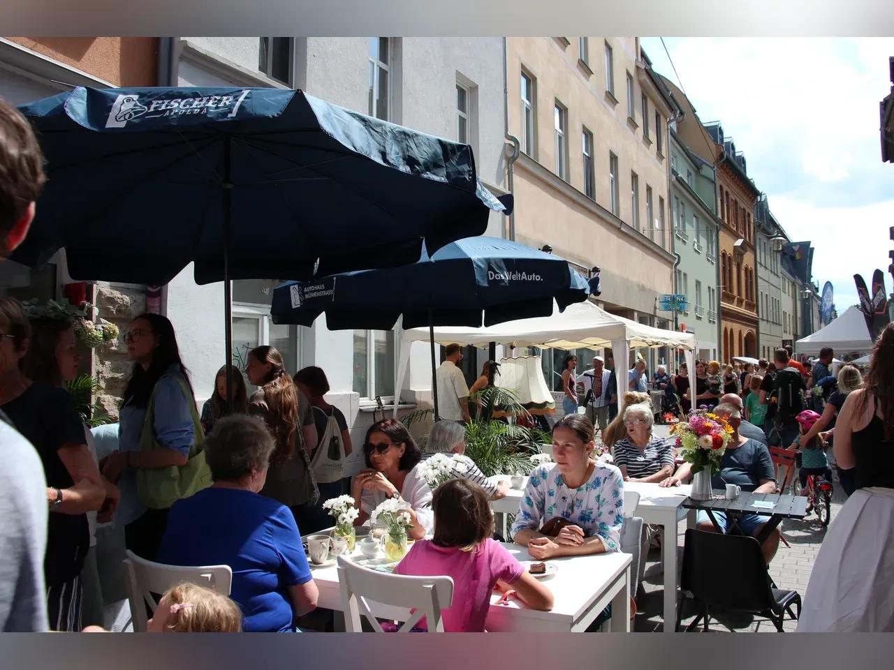 Besucher:innen sitzen und schlendern beim Neugassenfest in der sonnigen Neugasse in Jena.