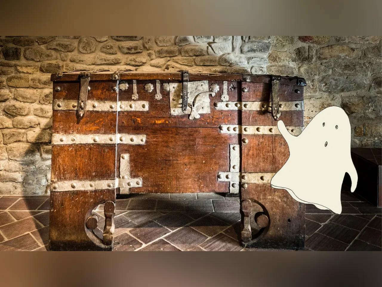 Gezeichnetes Gespenst vor mittelalterlicher Truhe in einem Raum mit Natursteinwand