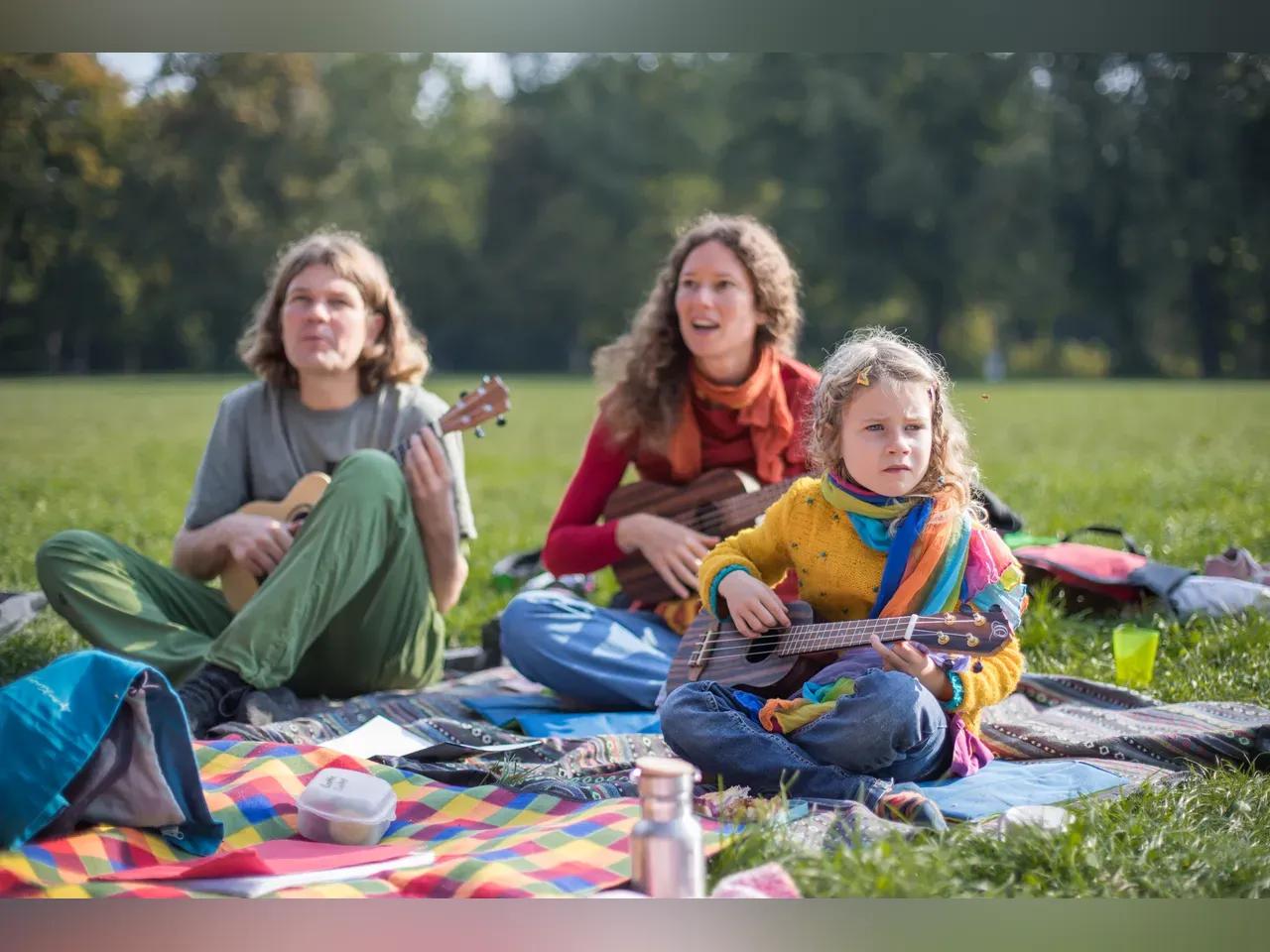 3 Personen (jung bis alt) sitzen im Park und spielen Ukulele