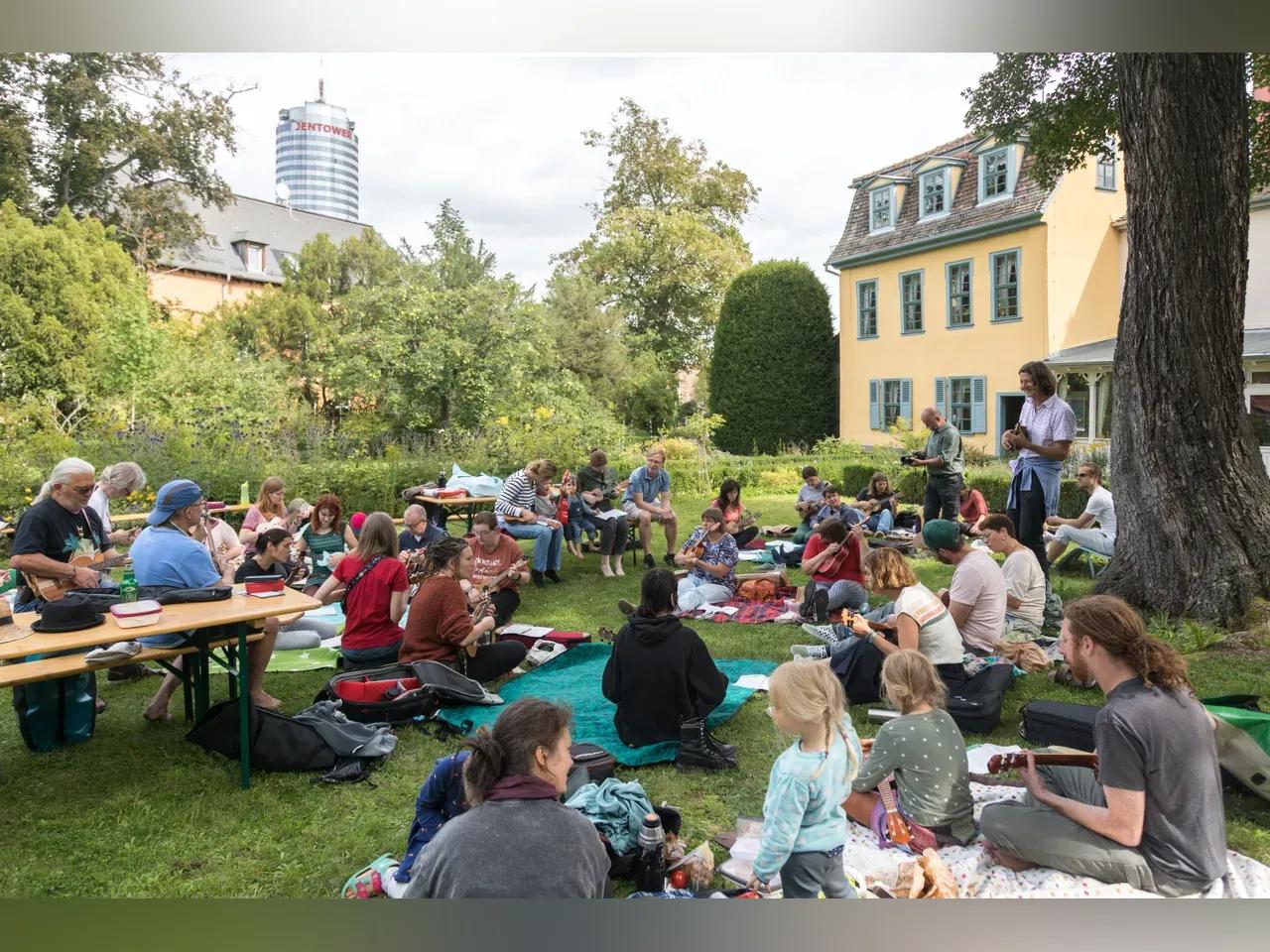 Menschen mit Ukulelen sitzen unter freiem Himmel und musizieren