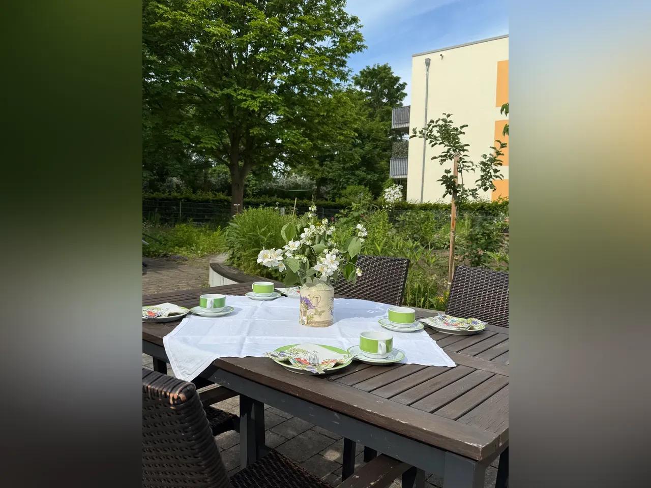 Gedeckter Tisch im Freien mit Tellern, Tassen und einem Blumenstrauß