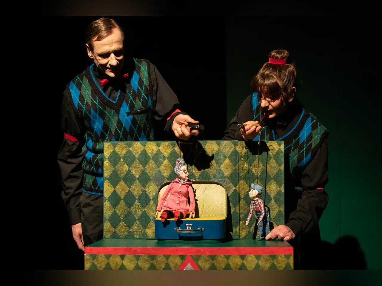 Bühnenbild von Oskar und die Dame in Rose: Puppenspieler:innen hinter einem Koffer, in dem eine rosa gekleidete Puppe sitzt