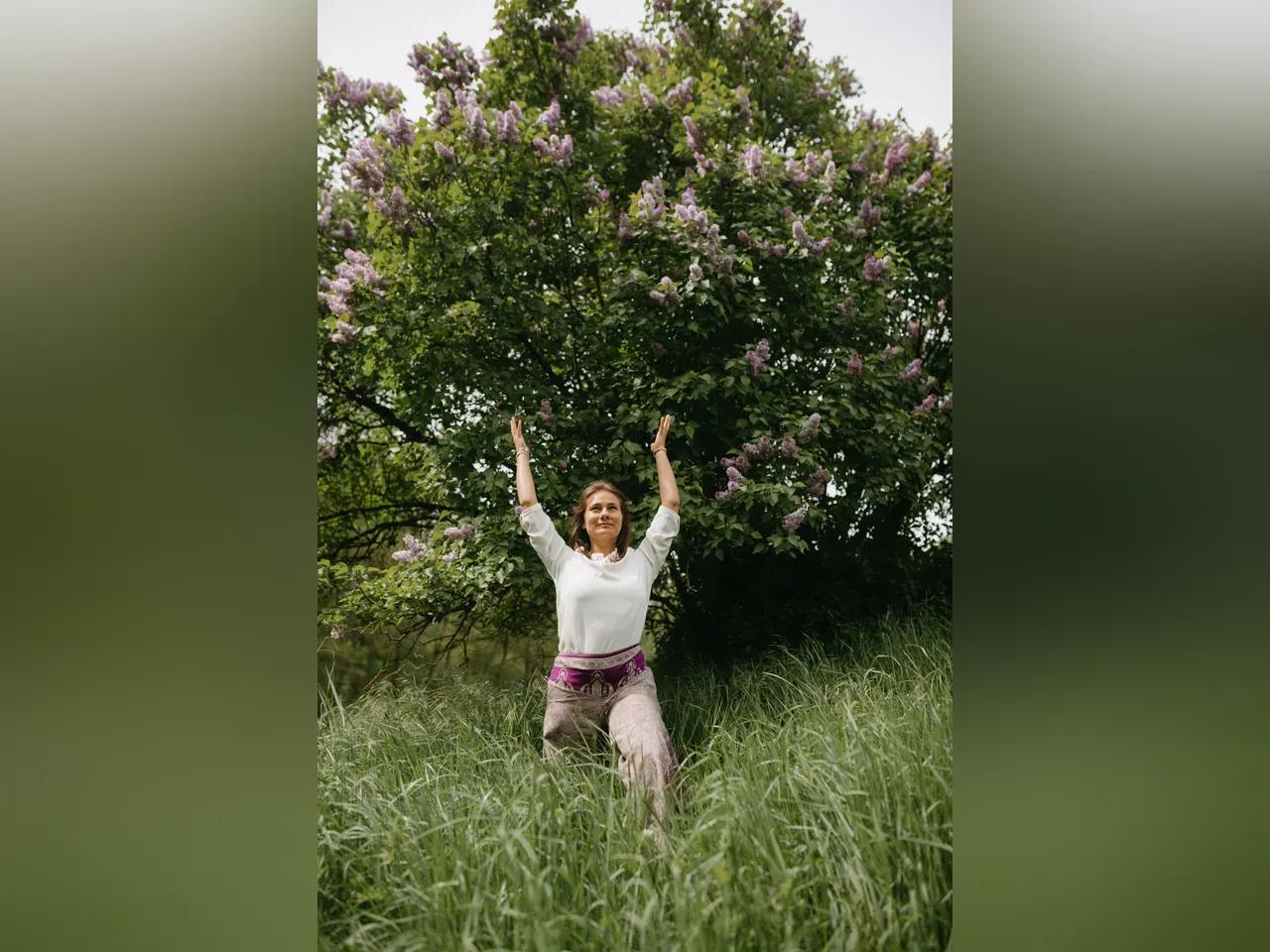Eine Frau macht eine Yoga-Übung im hohen Gras vor einem Baum