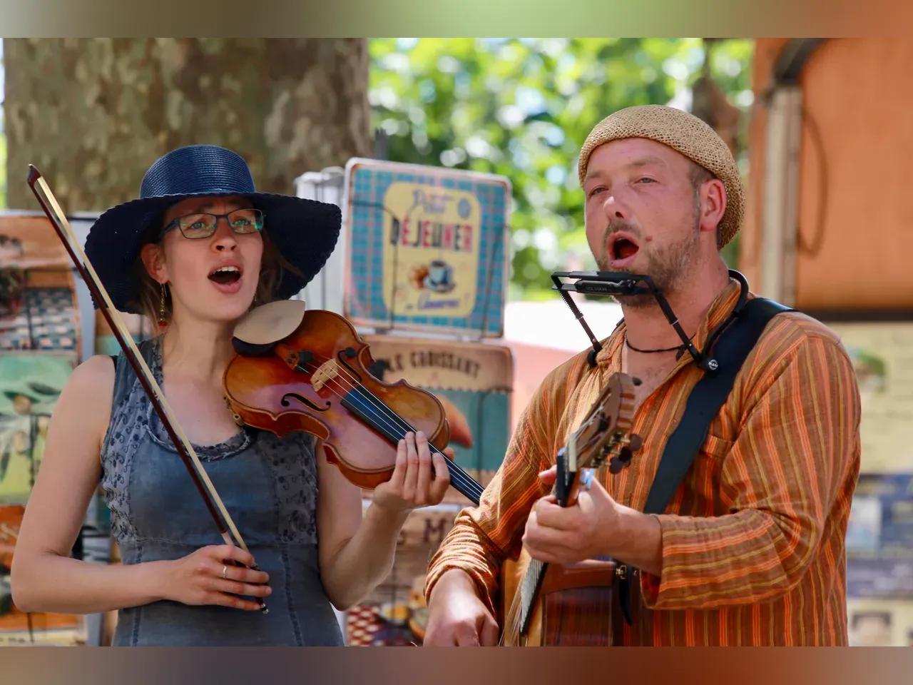 Eine Frau mit Geige und ein Mann mit Gitarre und Mundharmonika singen.