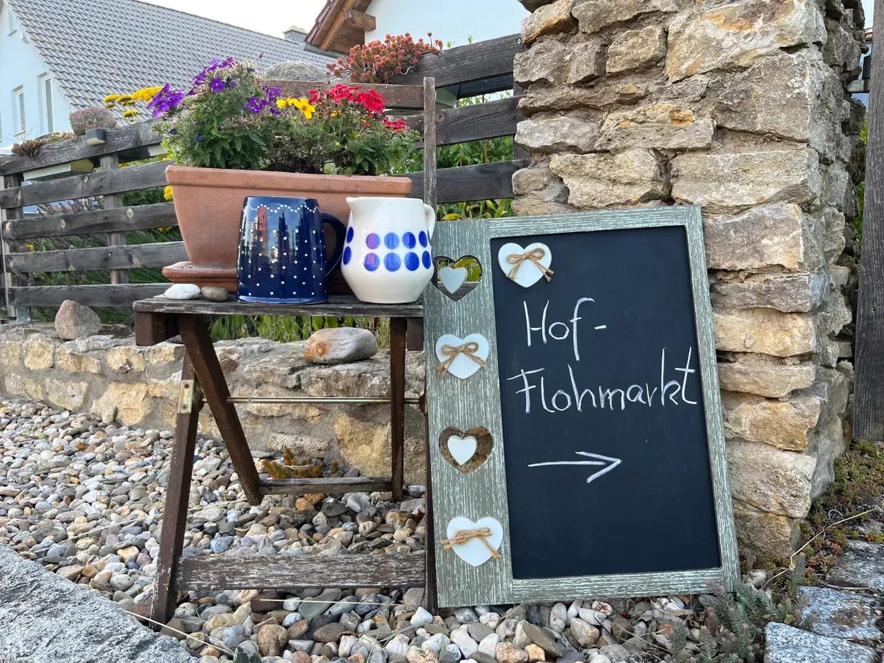 Hofeingang, schön dekoriert mit Stuhl, Blumen, Krügen und einer Tafel mit der Aufschrift "Hof-Flohmarkt"