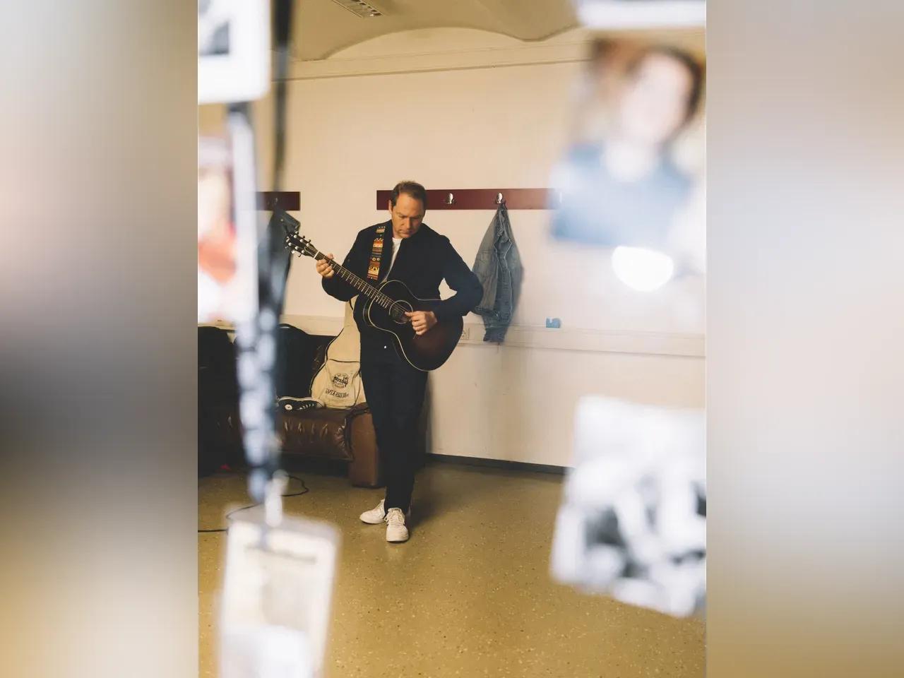 Thees Uhlmann mit Gitarre in einer Garderobe.