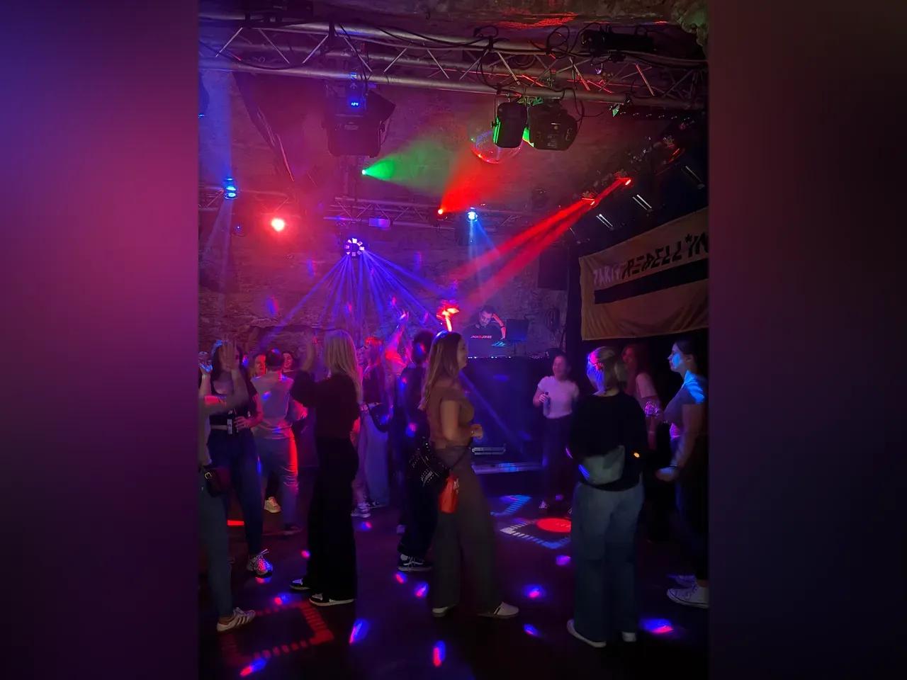 Junge Menschen tanzen auf einer Tanzfläche vor einem DJ-Pult